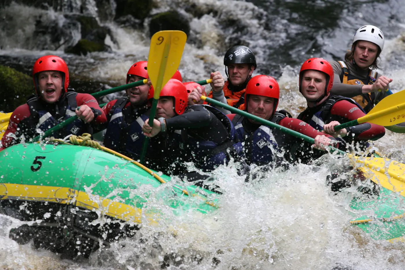 A group in red helmets paddling a raft through white water rapids in South Wales