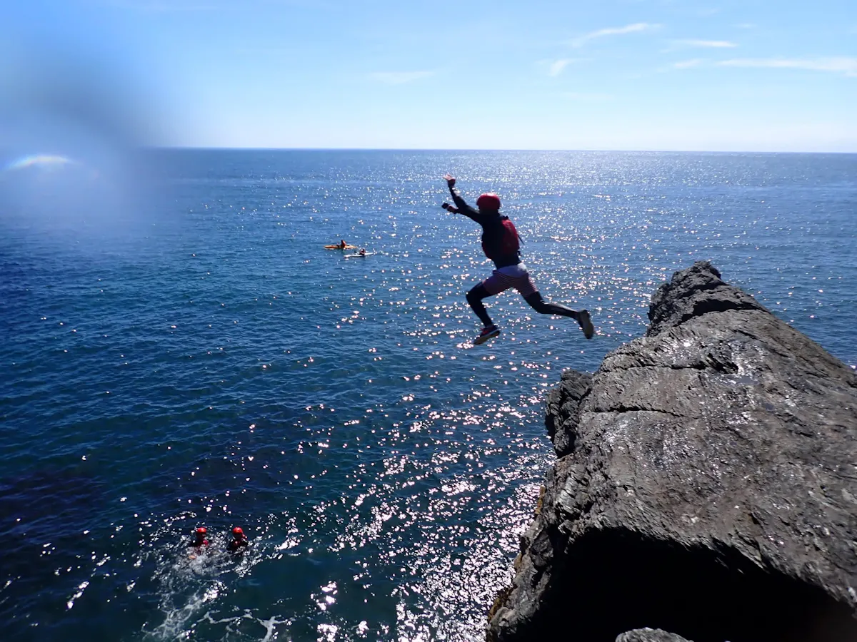A coasteerer in a helmet and buoyancy aid leaping off a rocky ledge into the sea on the Anglesey coast near Holyhead