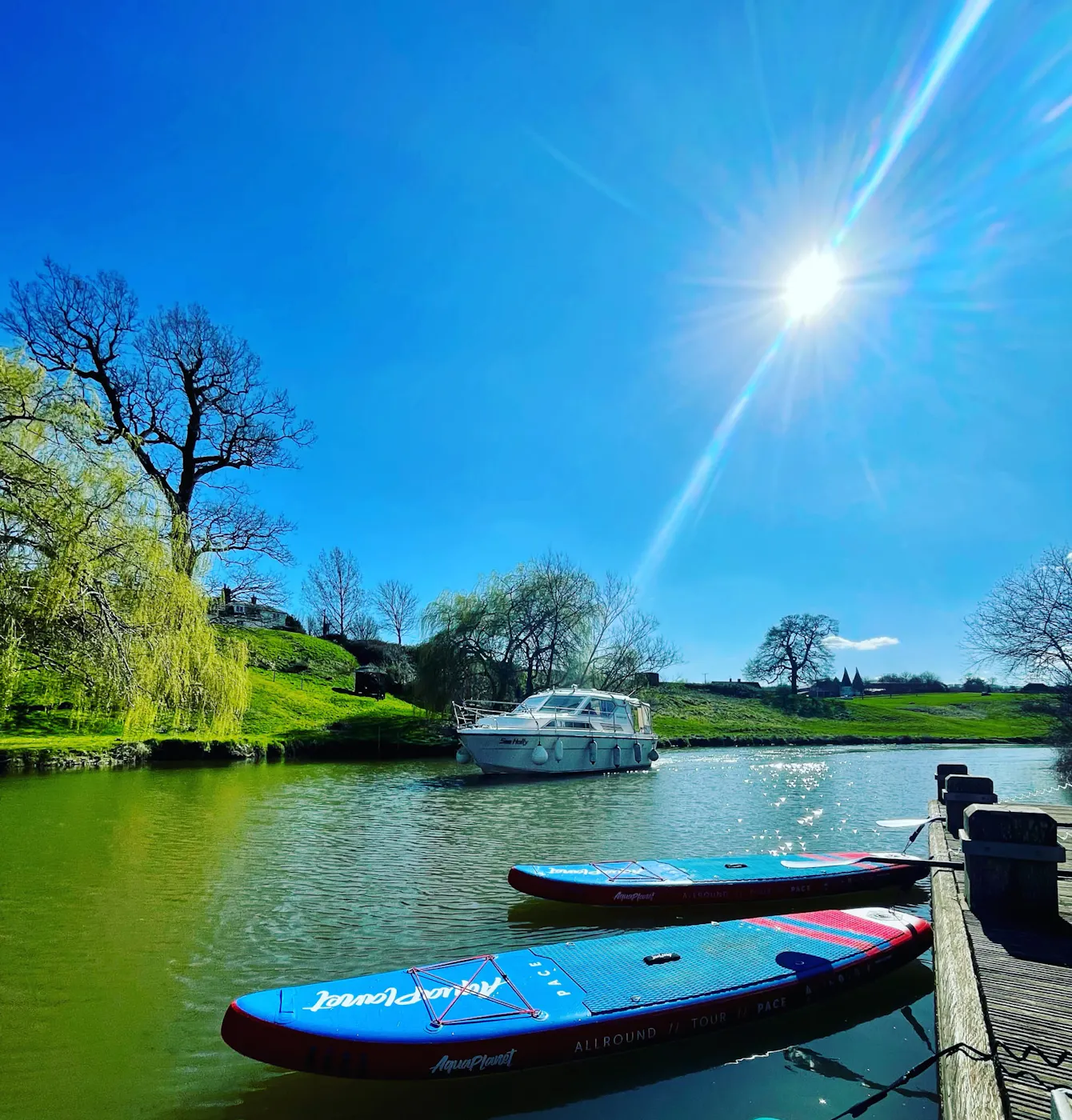 Two paddleboards moored at a wooden pontoon on a sunny river in Kent, with a motor cruiser behind