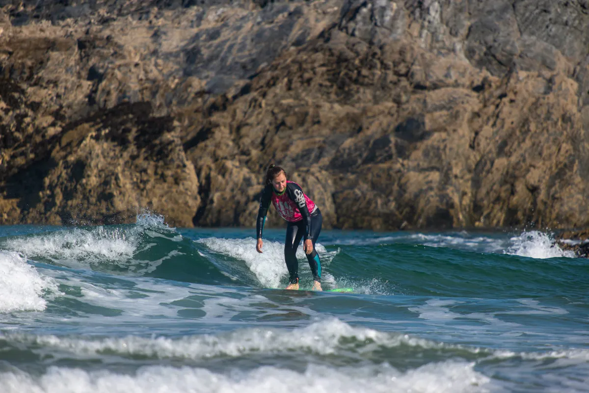 A surfer in a pink rash vest riding a small wave in front of the rocks at Crantock Beach in Cornwall