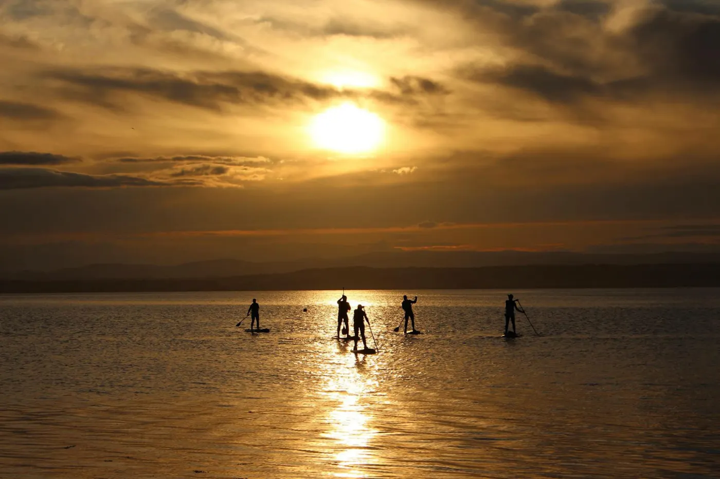 Paddleboarders silhouetted against a golden sunset on the east coast of Scotland