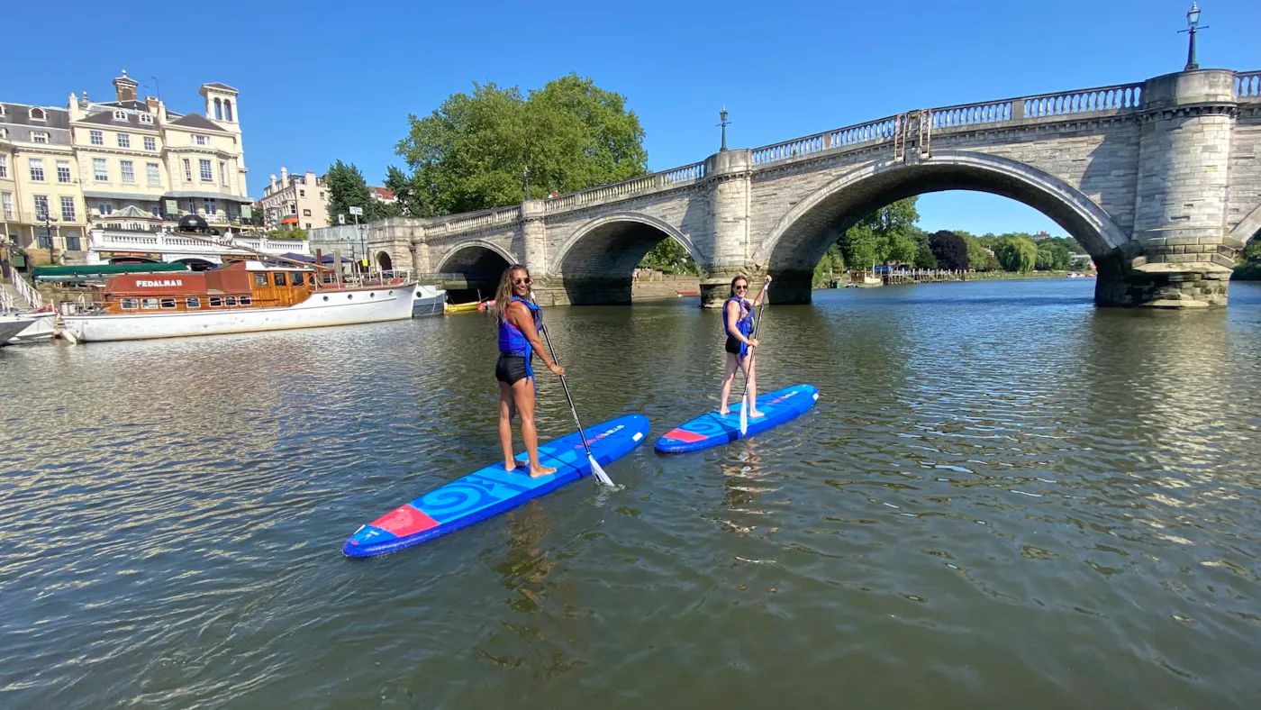Two paddleboarders on the River Thames beside Richmond Bridge