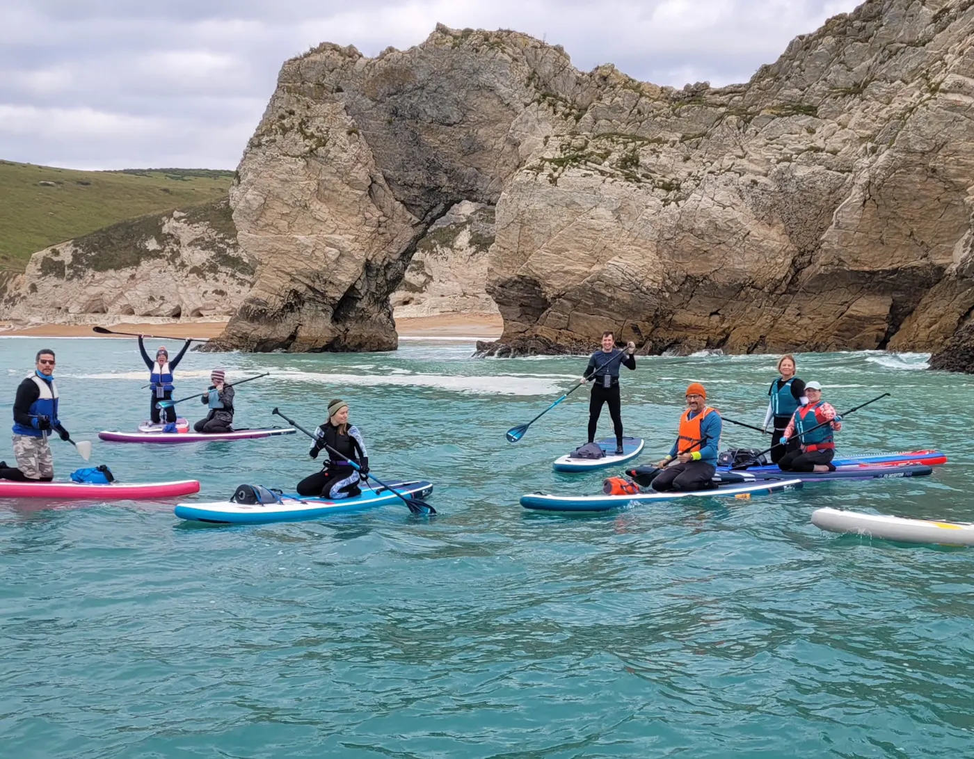 A group of paddleboarders on turquoise water beside Durdle Door on the Dorset coast