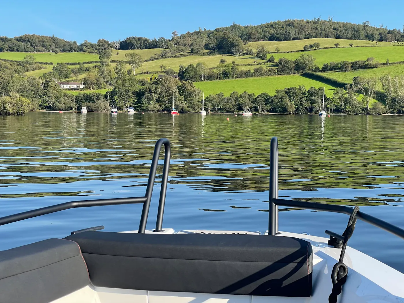 View from the bow of a speedboat towards green hills and moored boats on Loch Lomond