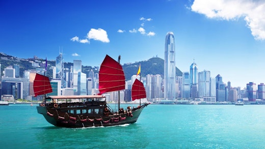 Vacker båt med röda segel, med Hongkongs skyline i bakgrunden.