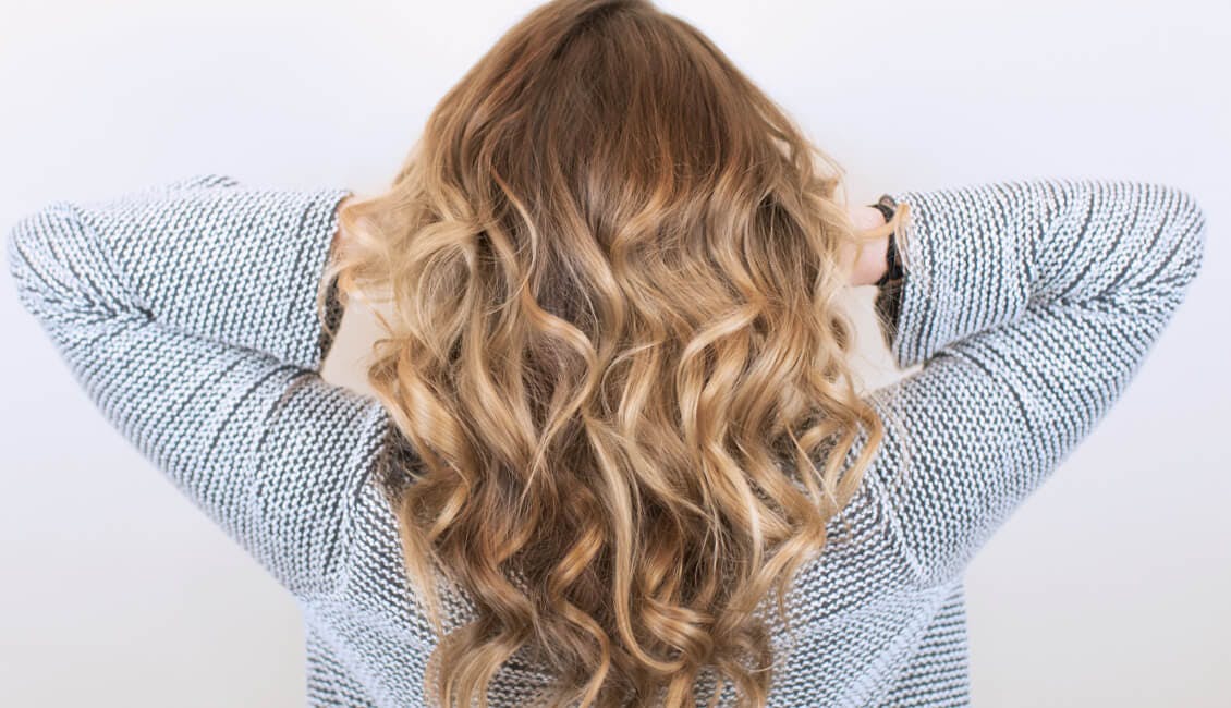 Image of esalon client back of head with custom toffee hair color and her hands in her curly hair