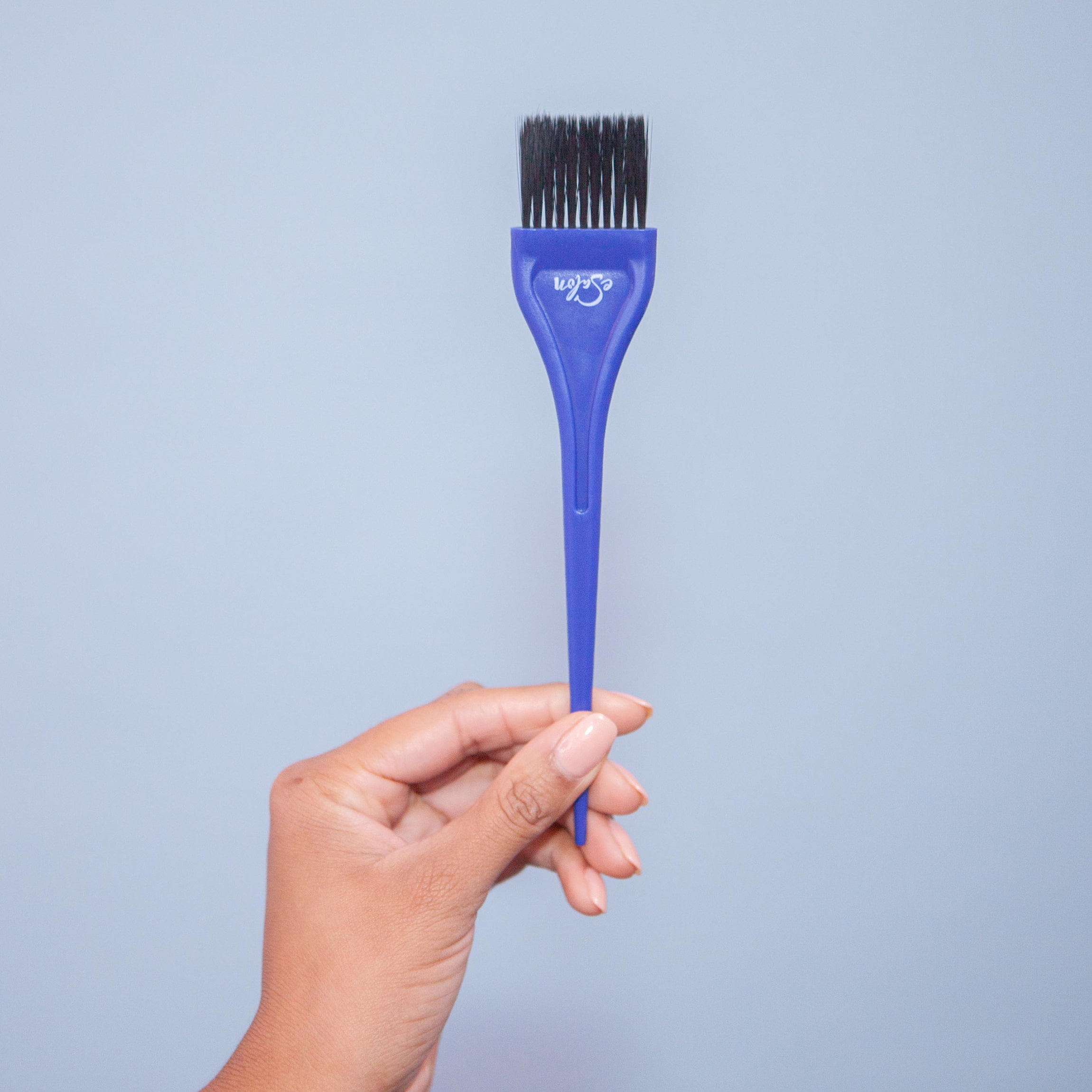 Image of esalon client's hand on phone to call their colorist on the right holding a tint brush