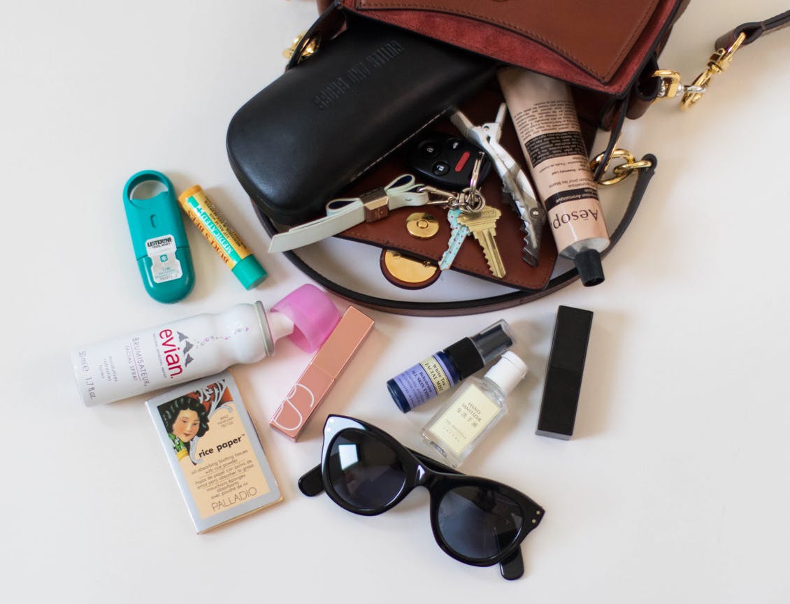 Image of esalon employee Jules' brown handbag spilled over with breath spray, evian facial spray, rice blotting papers, sunglasses, hand sanitizer, lipstick, perfume, burt's bees lip balm, aesop hand lotion tube and keys