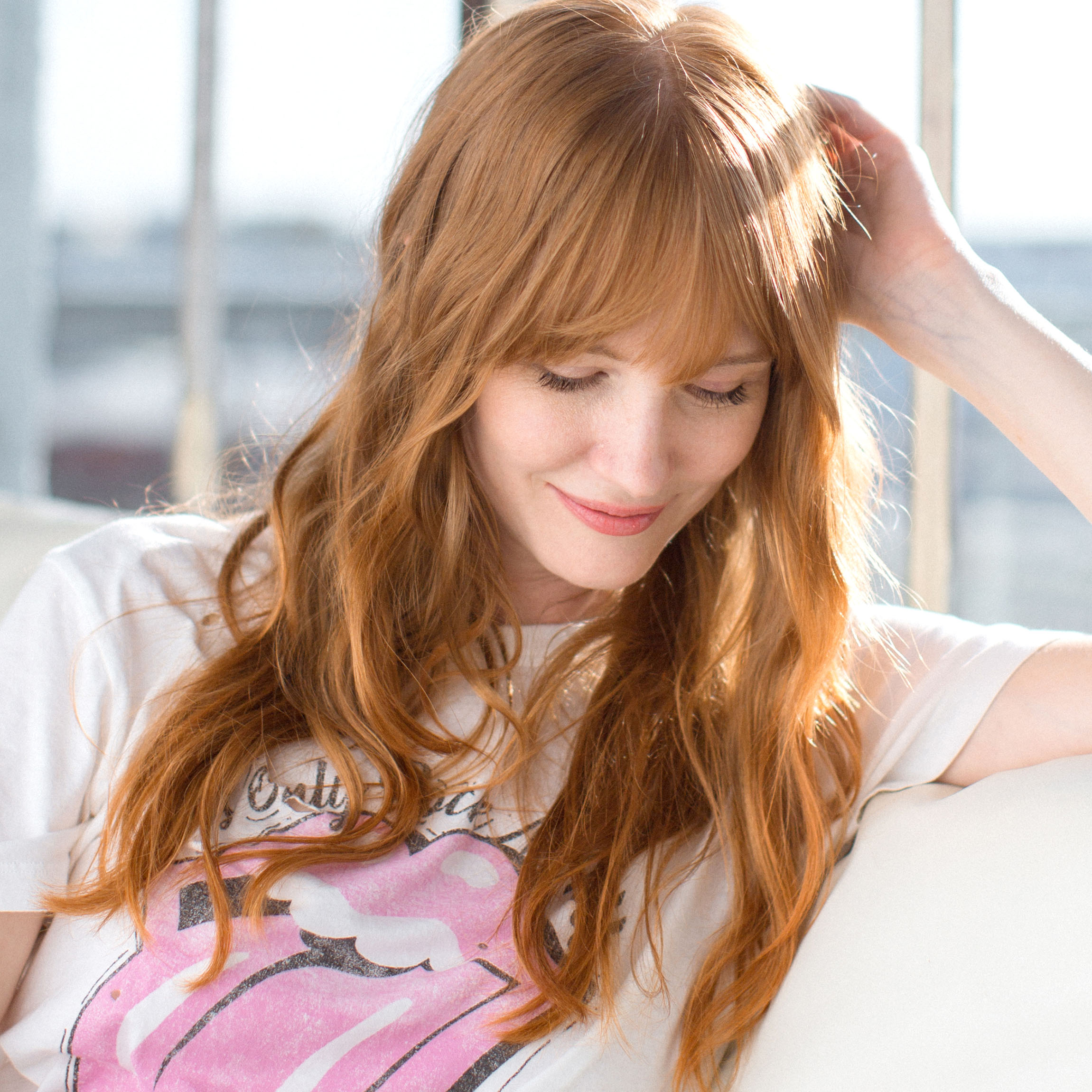 Image of woman with gorgeous red copper custom hair color sitting on a couch in the sunlight of a window nearby
