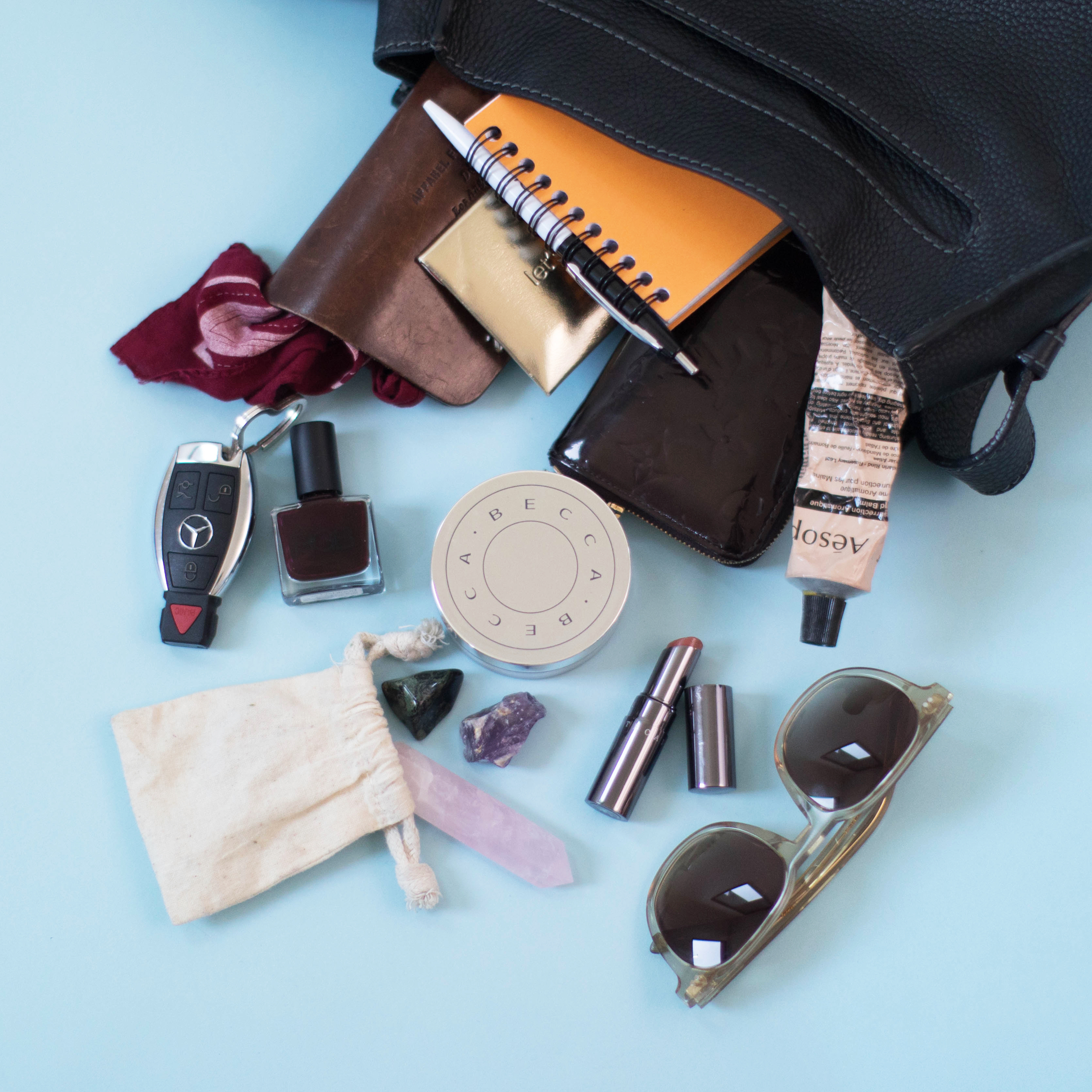 Carousel image of esalon employee handbags spilled over on a blue background to showcase beauty items inside