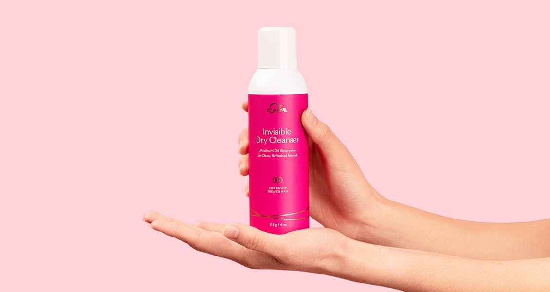 Studio image of Invisible Dry Cleanser spray bottle held on display in model's hands. 
