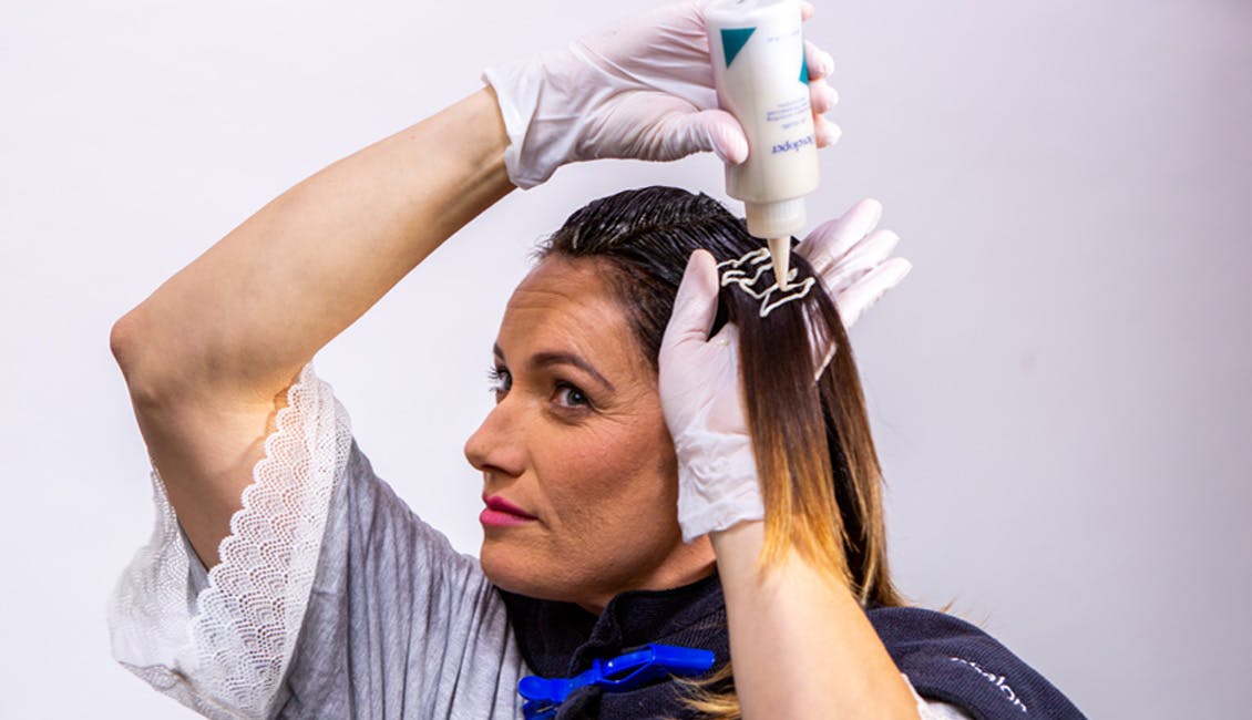 Woman with brunette hair using a bottle to color her hair at home.