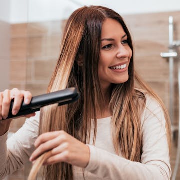 Woman with long brunette hair using a straightener.