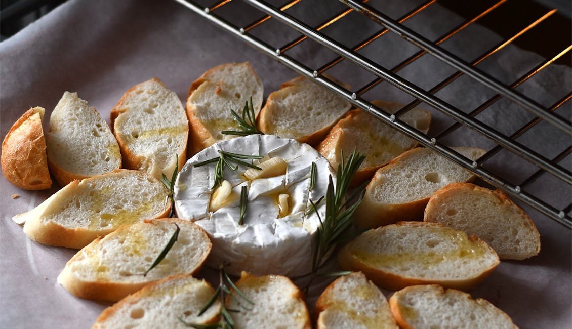 Wheel of brie cheese surrounded by sliced baguette ready to be placed in the oven. 