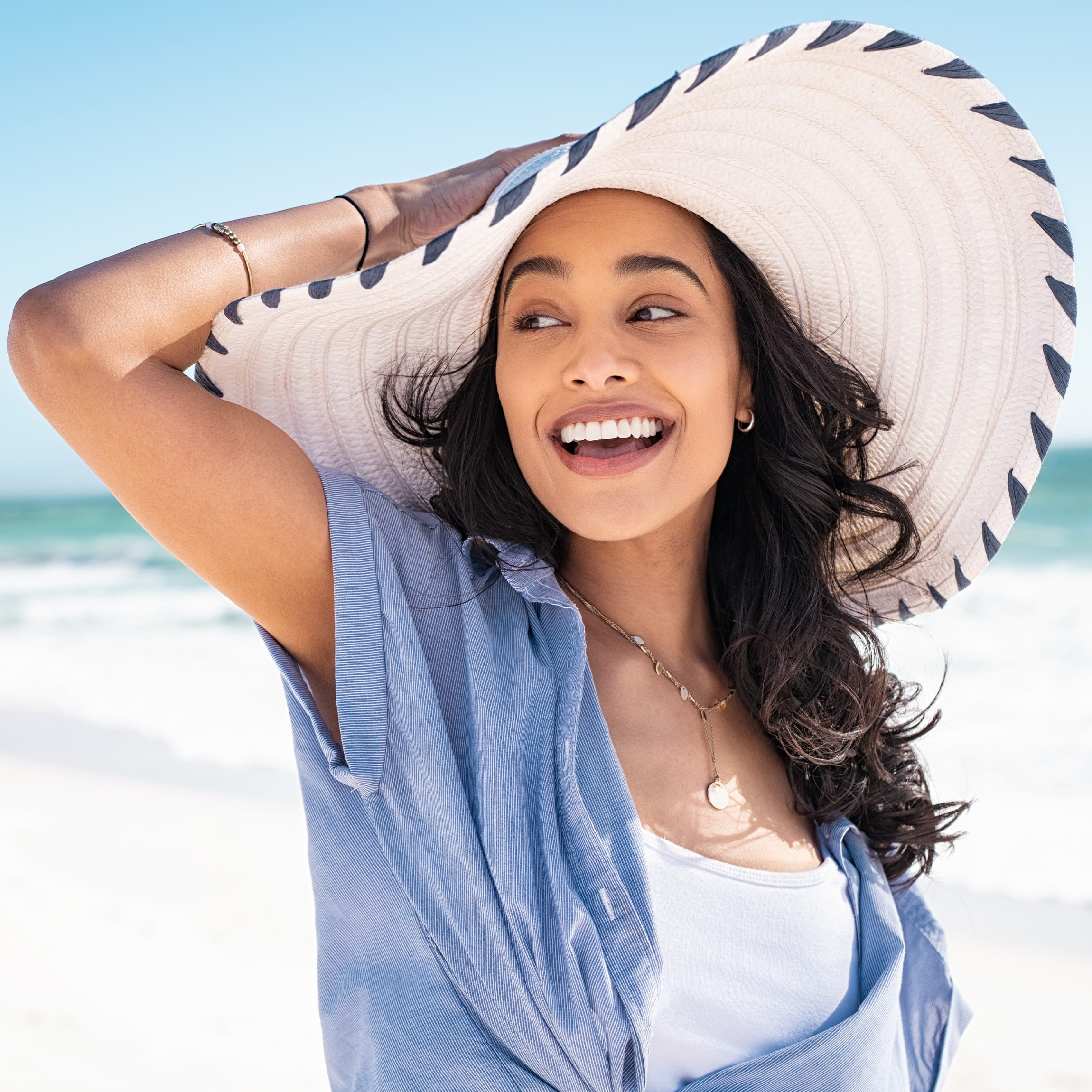 Woman with dark hair and a sun hat at the beach.