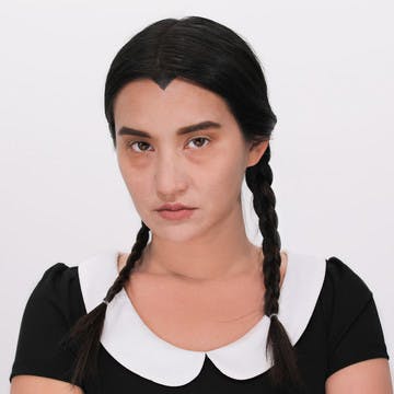 Hero image of an esalon employee dressed as wednesday adams featuring her holiday hairstyle with custom dark hair color
