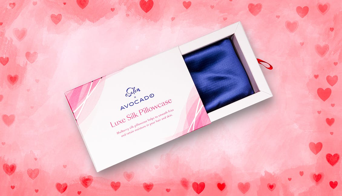 An open box showing a blue silk pillowcase with pink and red hearts in the background. 