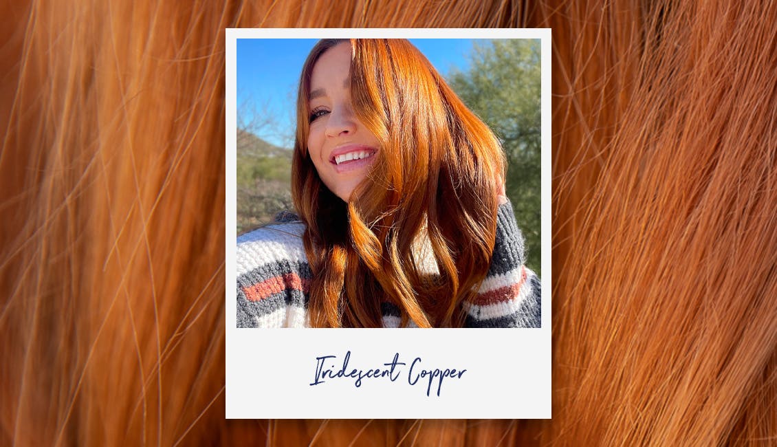 Woman smiling with flowing vibrant red hair outside.