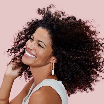  African american woman with dark curly hair smiling against a pink background
