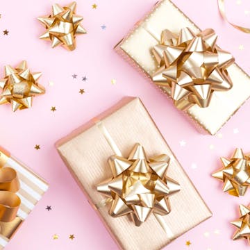 An array of gifts wrapped in gold, scattered on a pink table. 