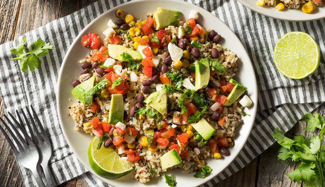 A bowl filled with brown rice, black beans, and the rest of the ingredients required to make a Veggie Burrito Bowl. 