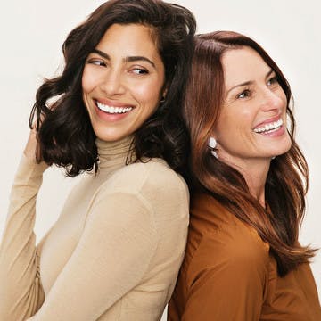 Image of two women laughing back to back, playing with their hair