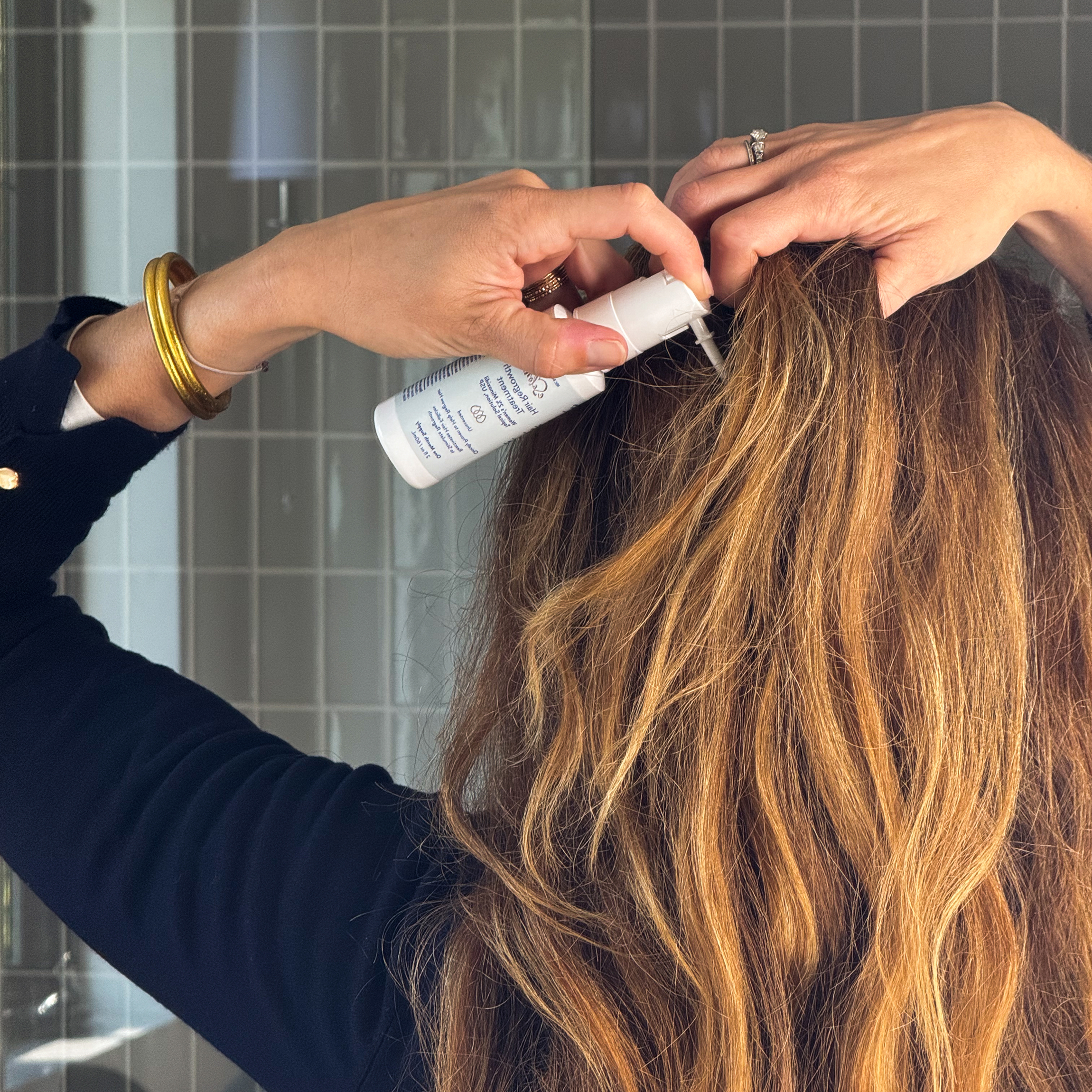 Back of a woman's head showing her applying eSalon's 2% minoxidil hair regrowth treatment directly to the scalp.