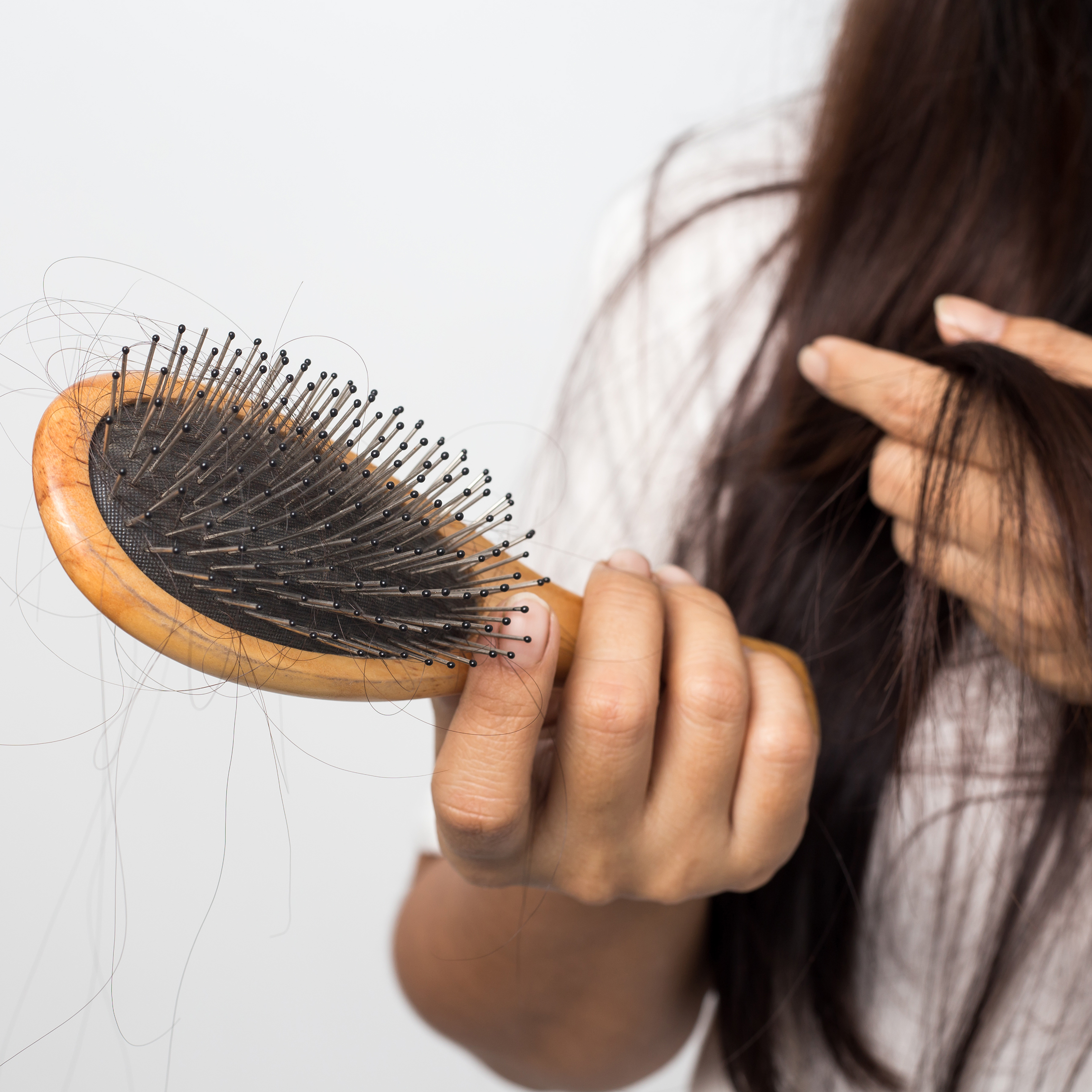 Woman brushing her long brunette hair and looking at hair in the brush.