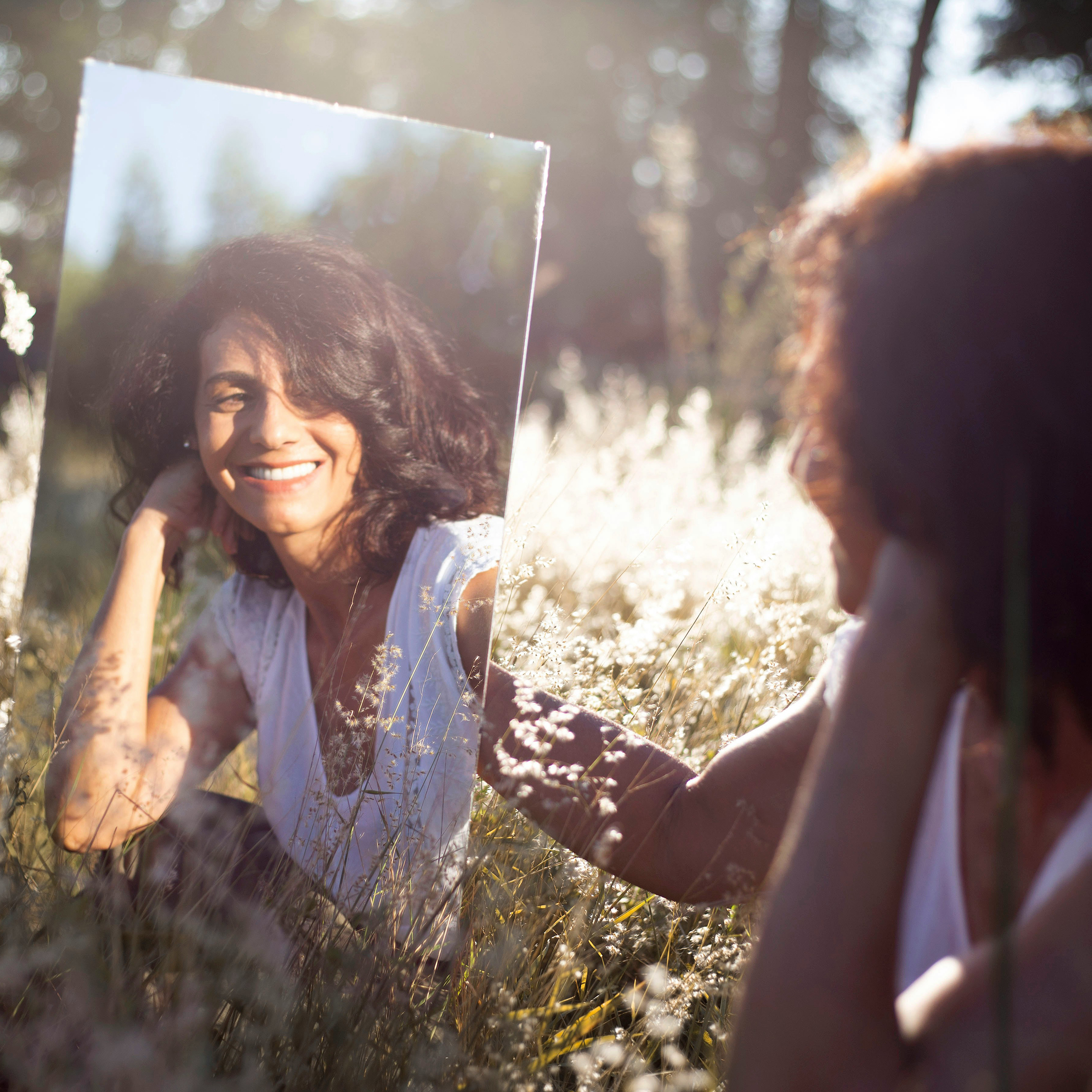 Woman with thick hair looking into a mirror and smiling. 