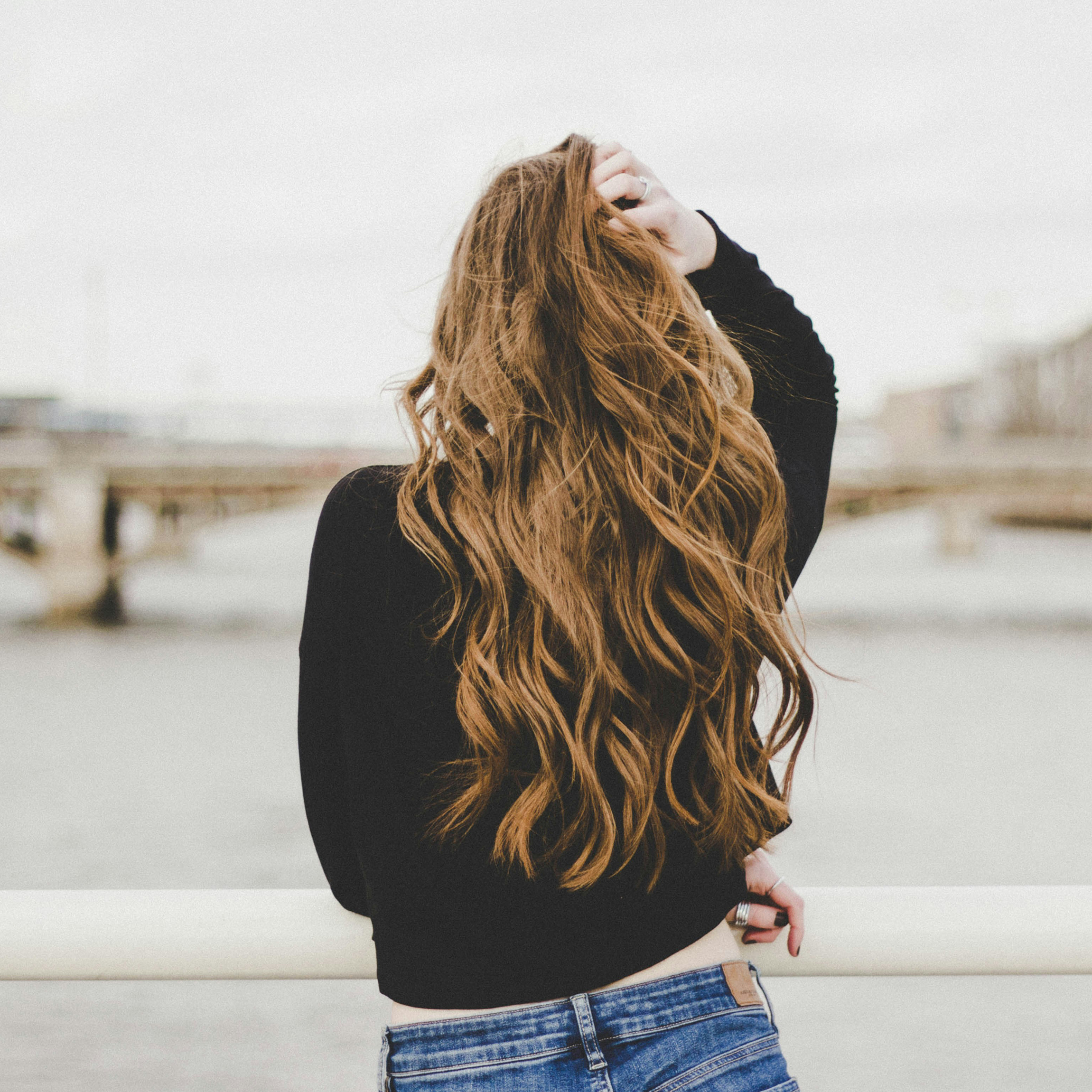 Back of woman's head and she is running her hands through her long hair. 