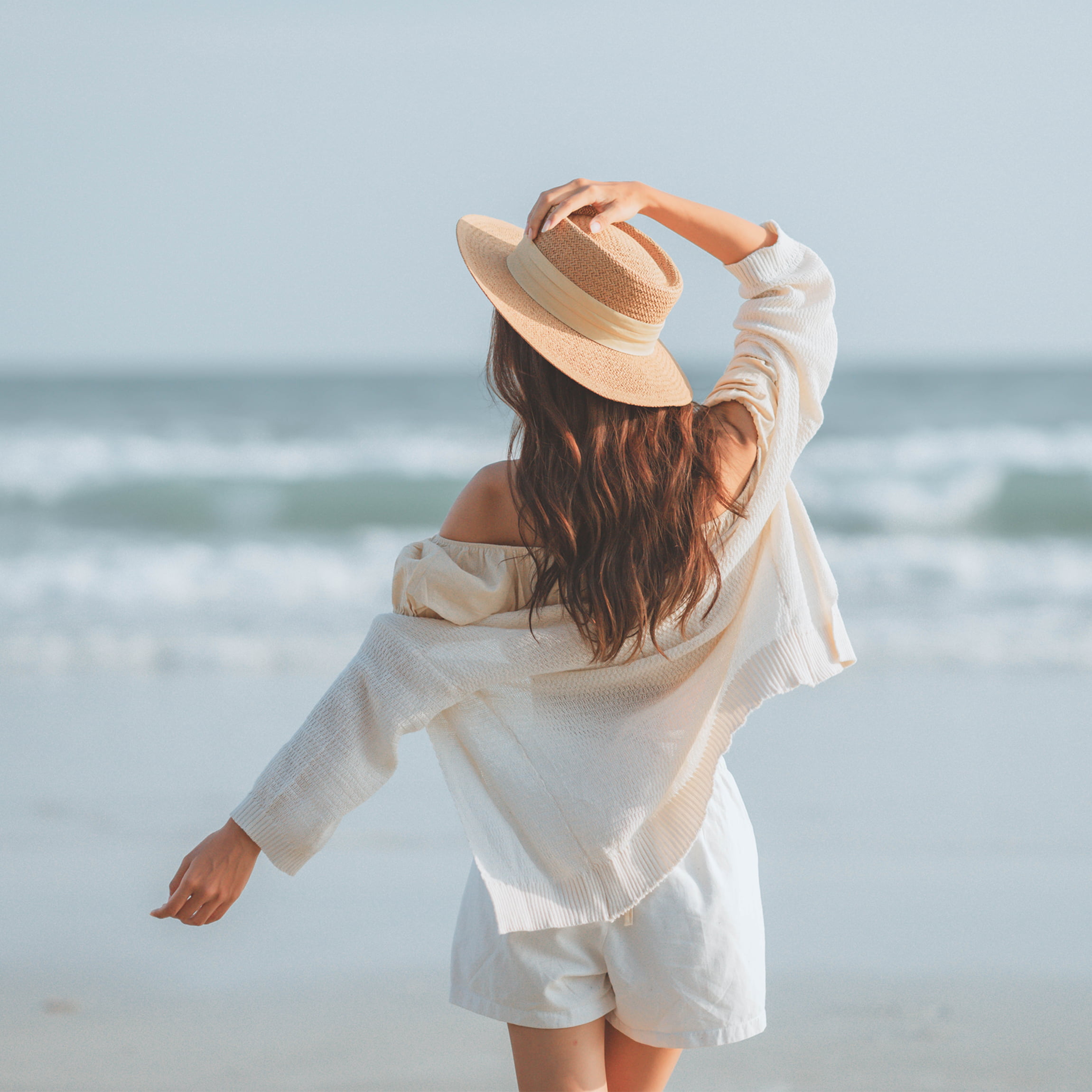Woman with long hair on the beach wearing a hat. 