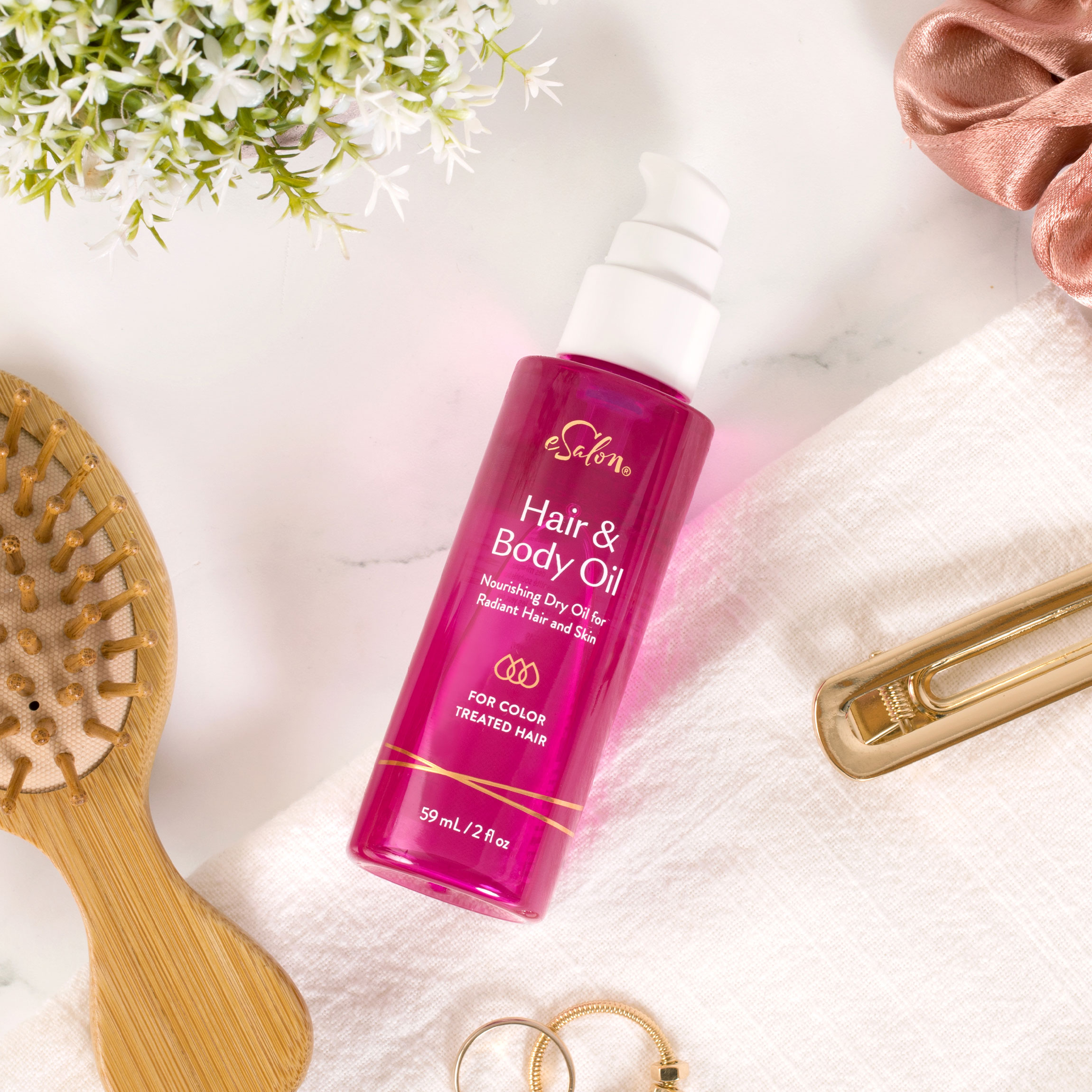 eSalon Hair & Body Oil on a counter with a hairbrush, clips, and a scrunchie. 