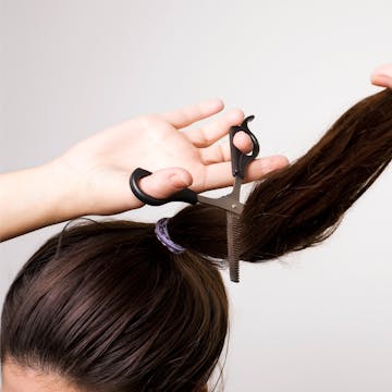 Woman cutting her own brunette hair with a pair of scissors.