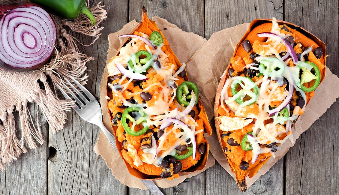 Two baked sweet potatoes filled with chili and topped with jalapeno, cheese, and onion. 