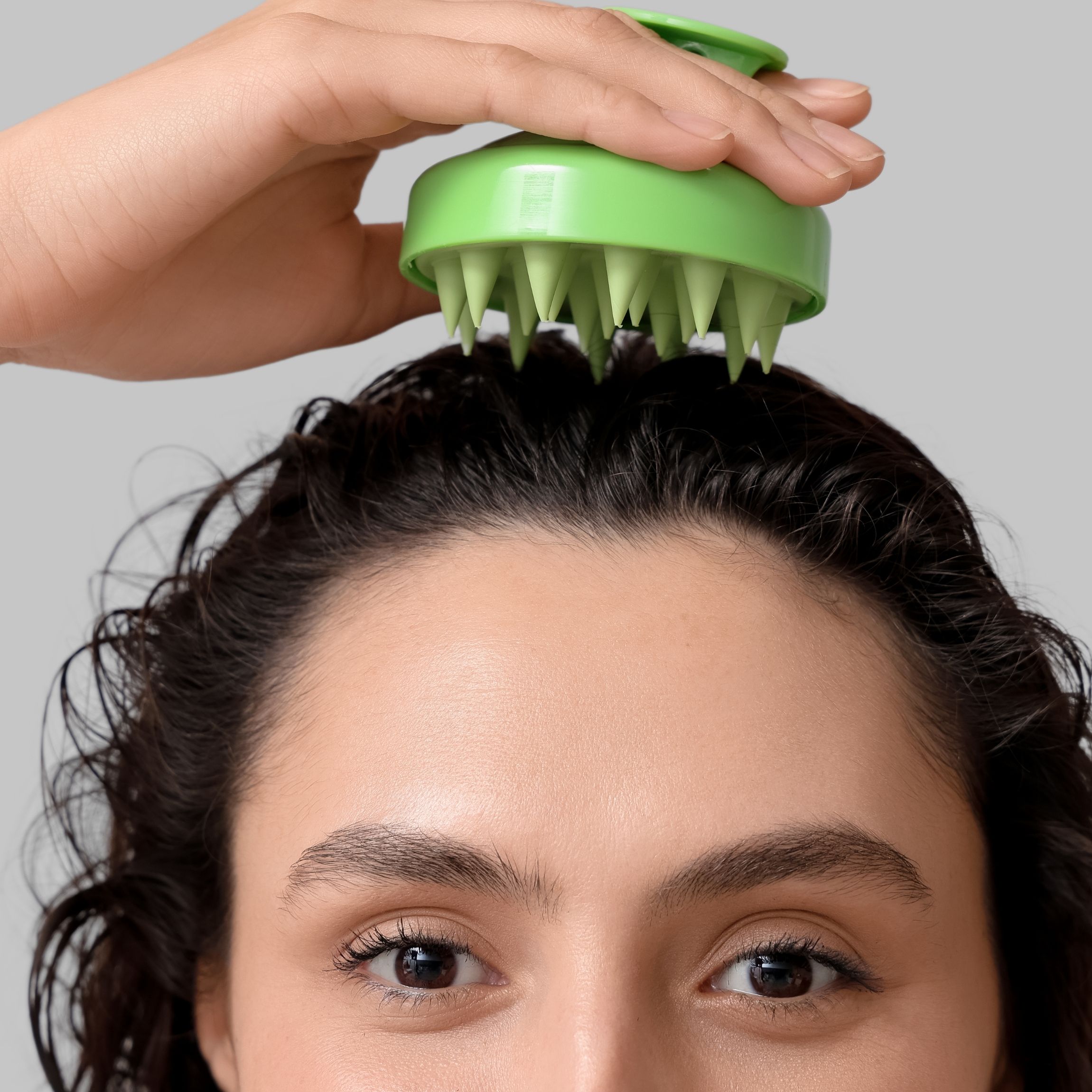 Woman with curly hair using a scalp massager. 