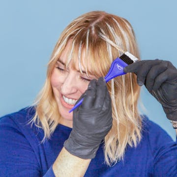 Blonde woman highlighting her hair with an application brush.