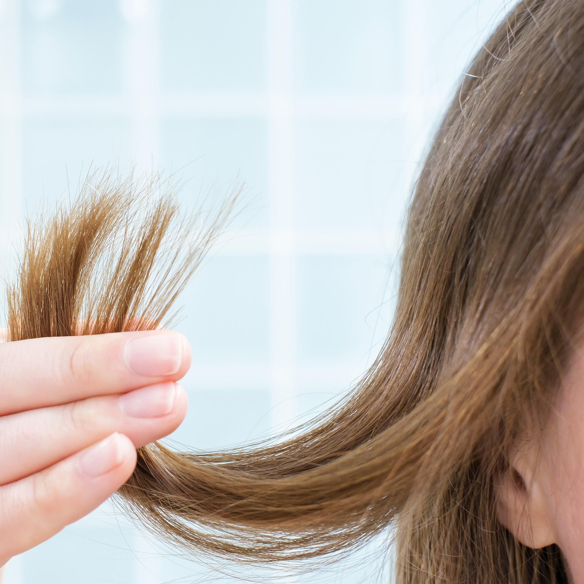 Woman with blonde hair examining the ends of her hair. 