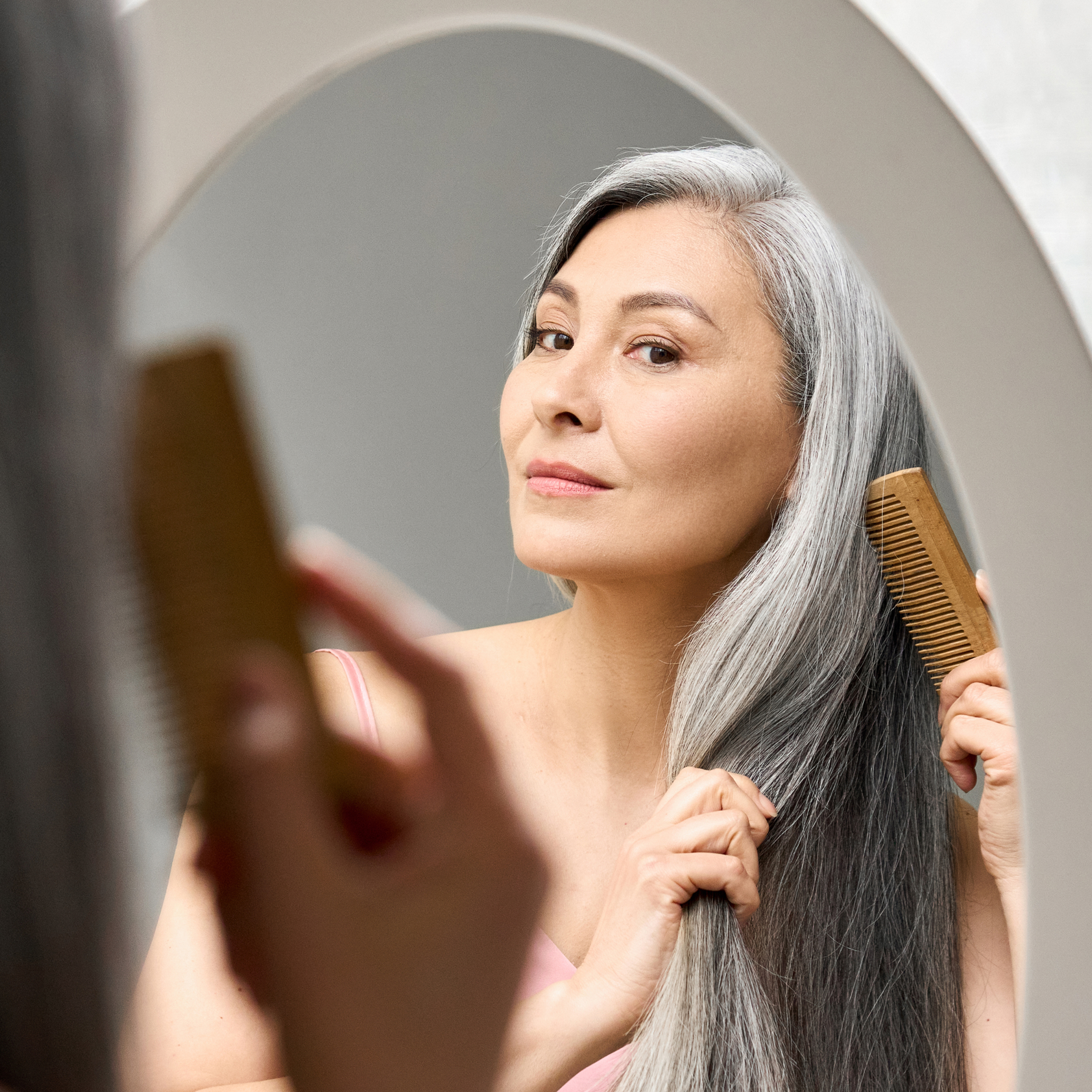 Woman combing her gray hair and looking in the mirror.
