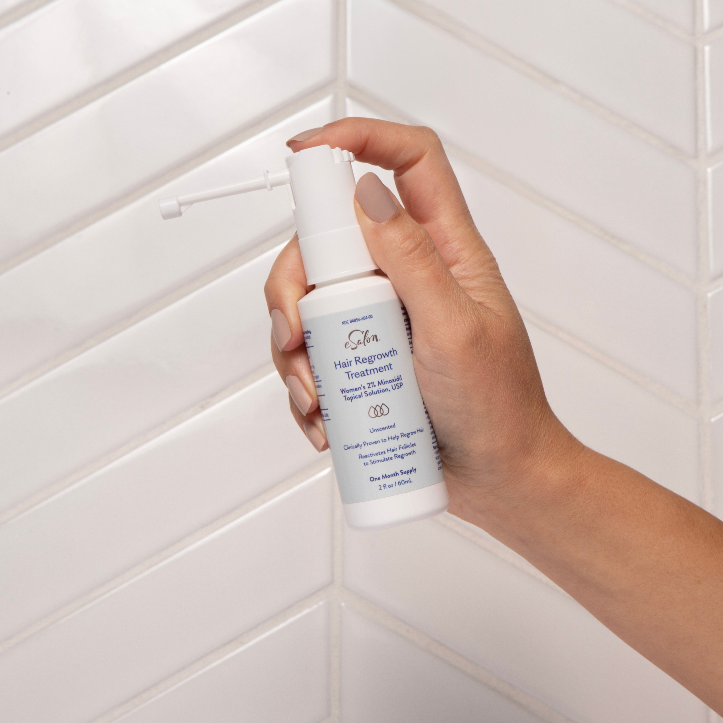 Person holding the 2% Minoxidil eSalon Hair Regrowth Treatment in front of a bathroom wall. 