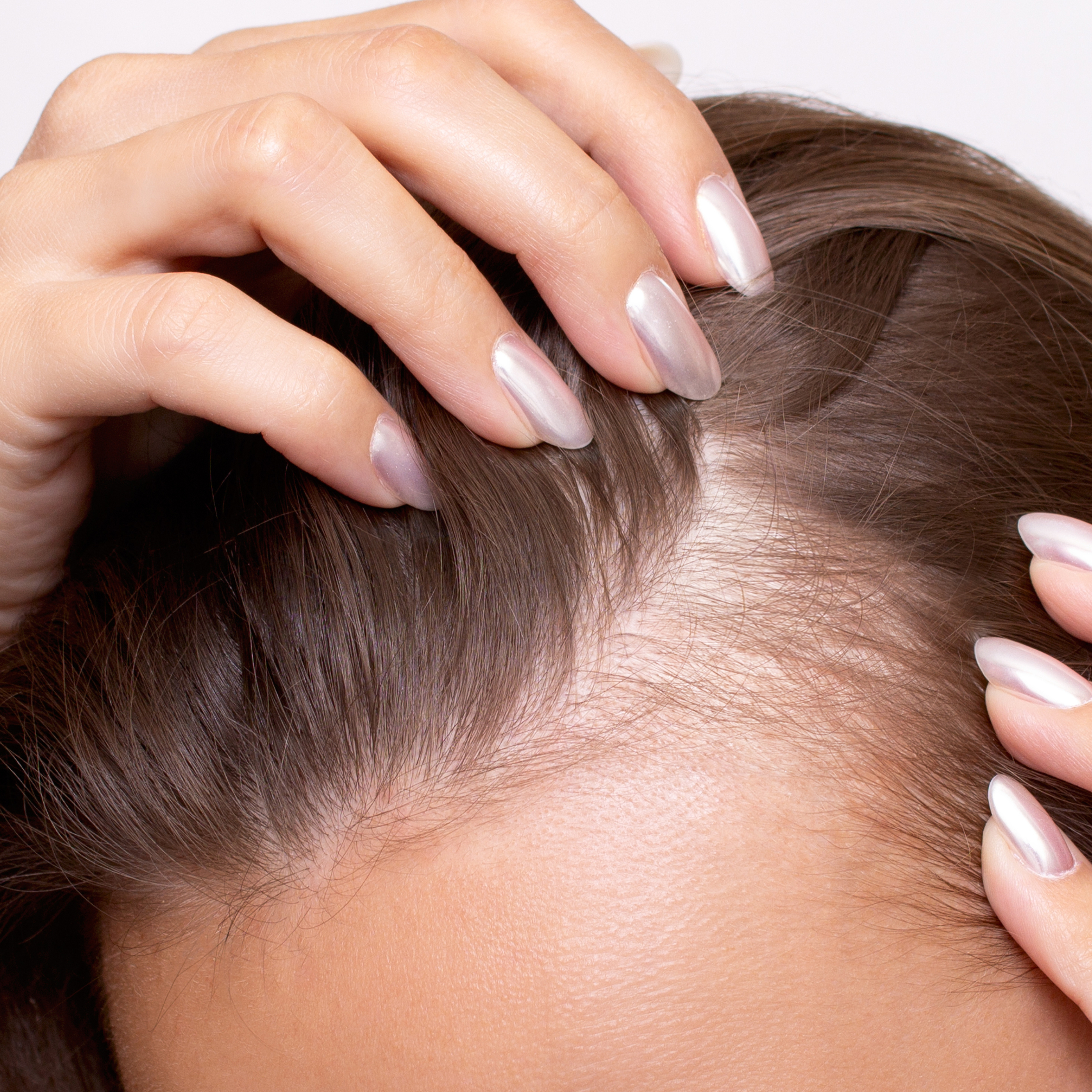 Up close image of a woman examining her scalp with her fingers. 
