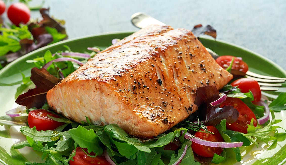 Cooked salmon on top of a green salad with tomato. 