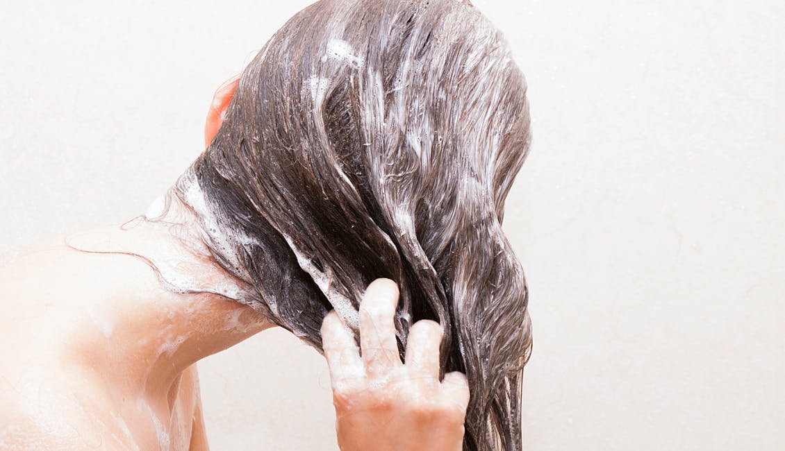 Woman washing her hair with color-loving eSalon shampoo and conditioner while rinsing her hair with cool water. 