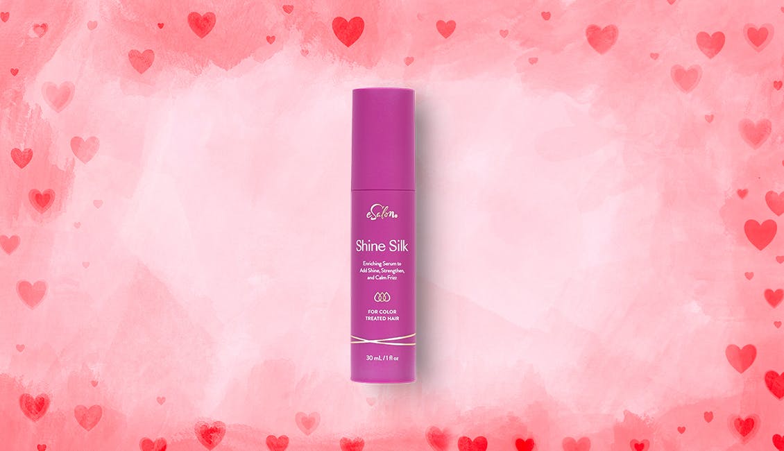 A tube of Shine Silk shine serum with pink and red hearts in the background. 