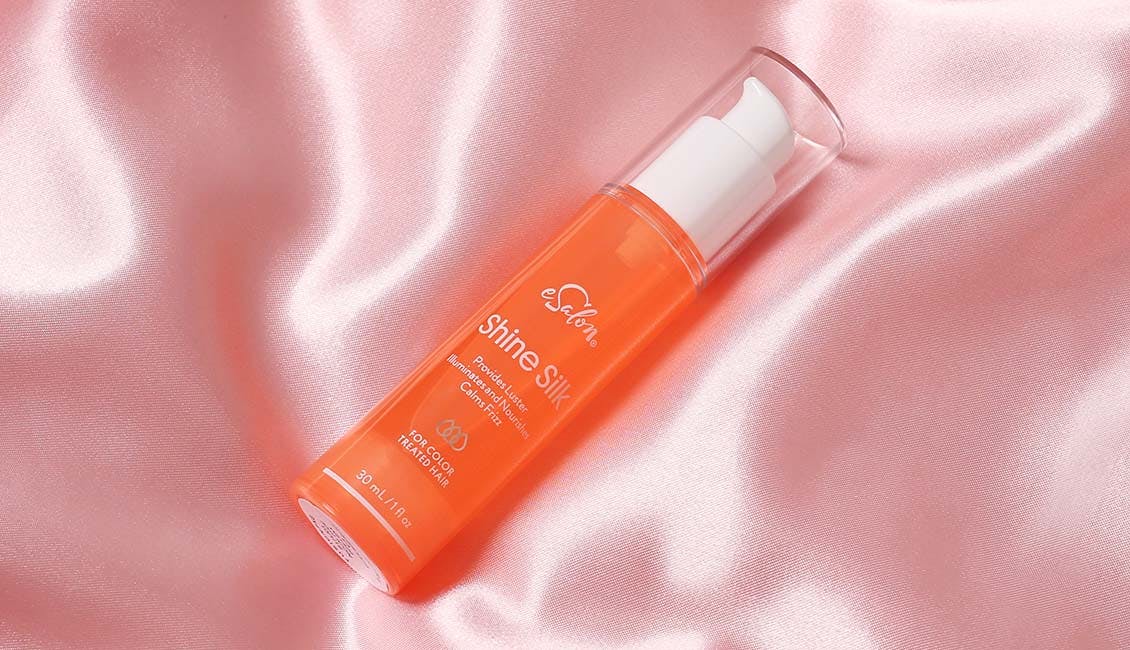 One orange bottle of Shine Silk laid atop a silky, pink-hued silk fabric.