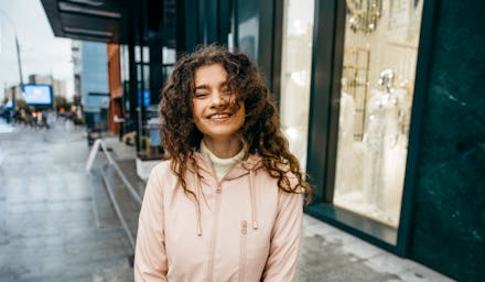 A woman smiles at the camera on a rainy day on a city street