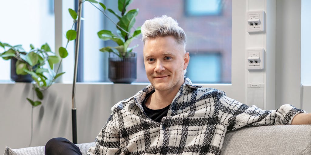 A blond man sitting on a couch in front of a window.