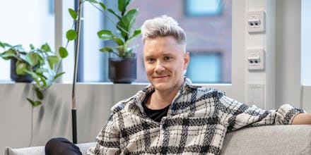 A blond man sitting on a couch in front of a window.