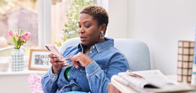 woman sat on armchair with package in knee and smartphone in hand