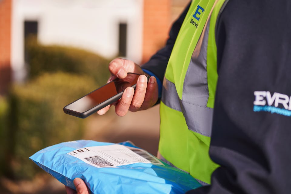 Photo of a courier scanning parcel with smartphone outdoors