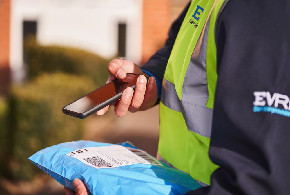 Photo of a courier scanning parcel with smartphone outdoors